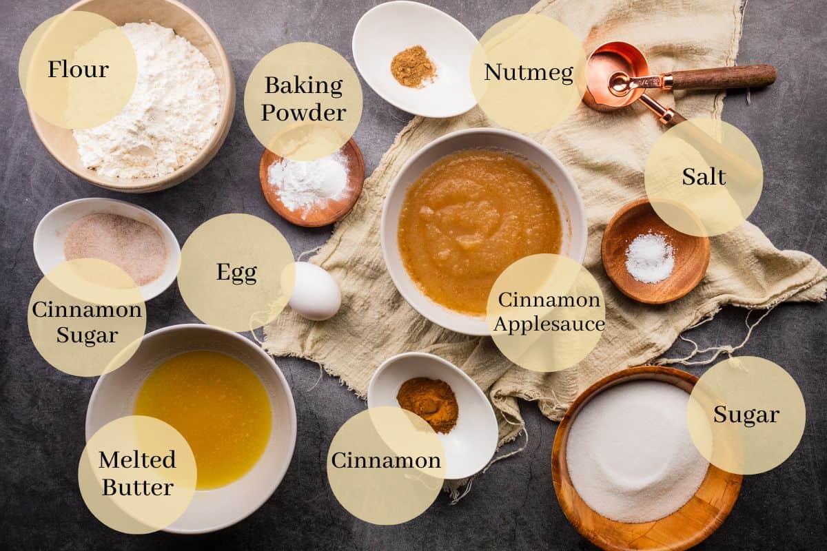 flour, baking powder, salt, cinnamon, nutmeg, egg, applesauce, sugar and melted butter on a table.