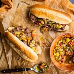 italian beef sandwiches topped with giardiniera on a cutting board.