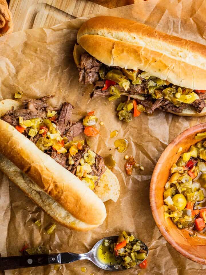 italian beef sandwiches topped with giardiniera on a cutting board.