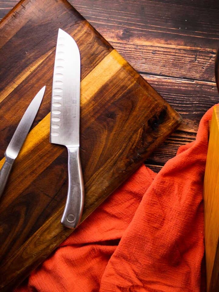 knives on a cutting board next to a knife block filled with knives.