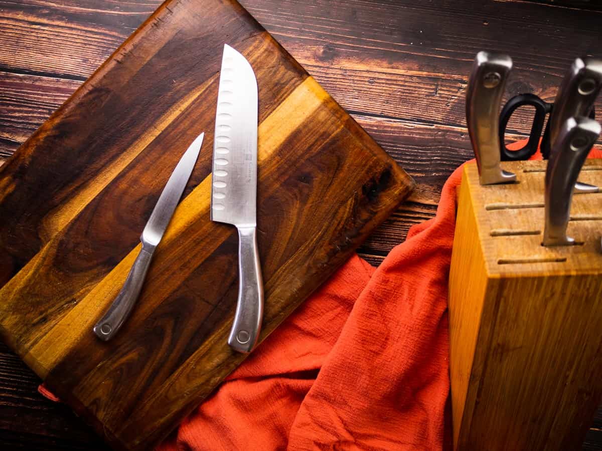 chefs knife and paring knife on a cutting board next to a knife block with other knives.