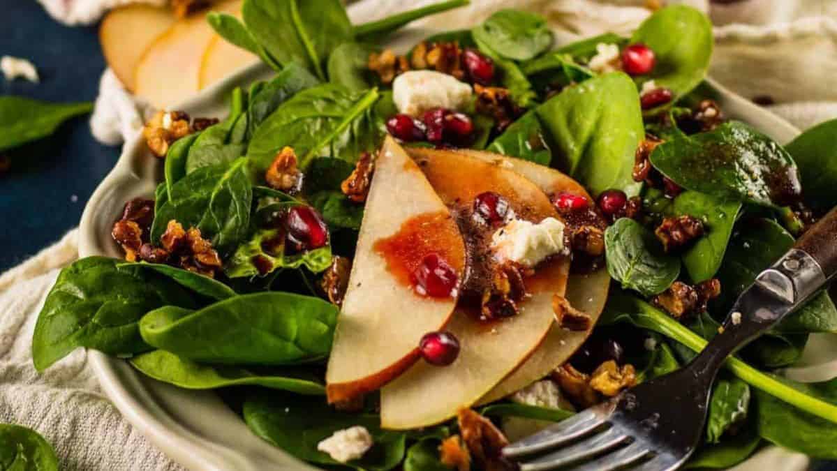 spinach salad topped with pears, pomegranate, cheese, nuts and dressing.