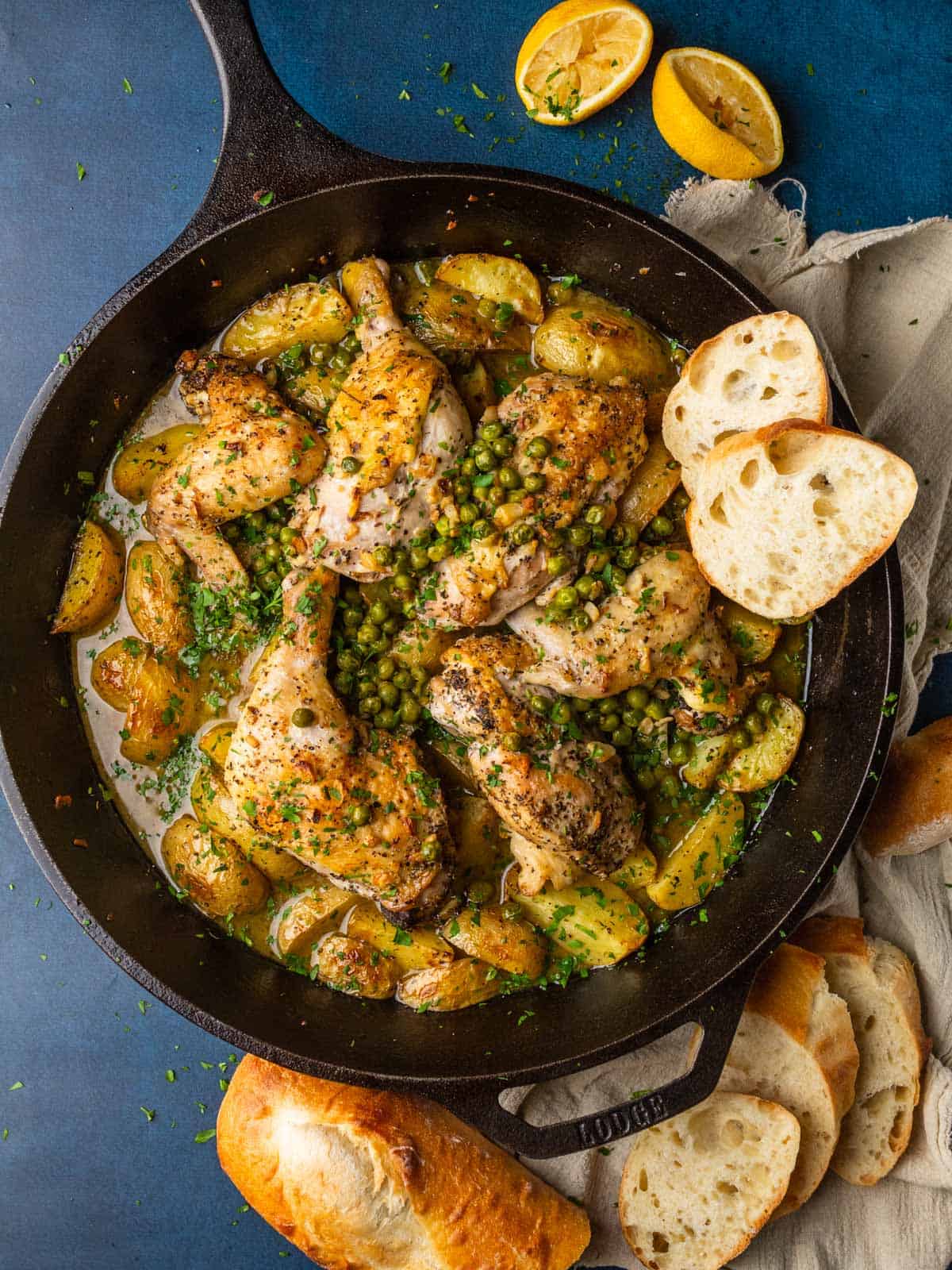 cast iron skillet with roasted chicken potatoes and peas in a sauce with a few slices of bread.