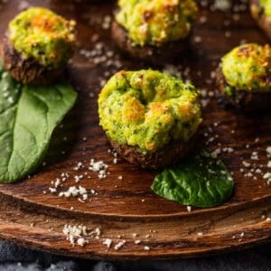 spinach and ricotta cheese stuffed mushrooms on a wooden tray with fresh spinach around.