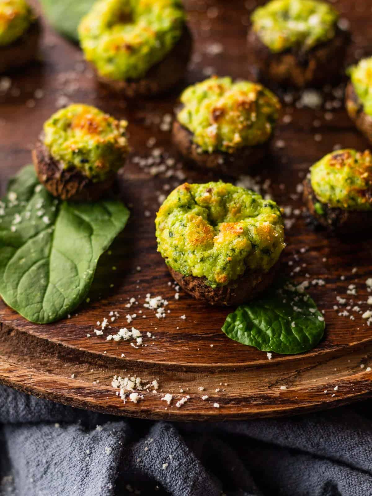 ricotta and spinach stuffed mushrooms on a wooden tray with fresh spinach leaves and sprinkled cheese.