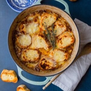 dutch oven pot with french onion soup topped with cheesy bread slices with bowls and spoons.