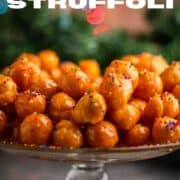 struffoli honey balls with sprinkles on a platter with christmas lights behind.