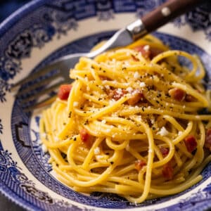 spaghetti carbonara topped with grated cheese in a blue bowl with a fork.