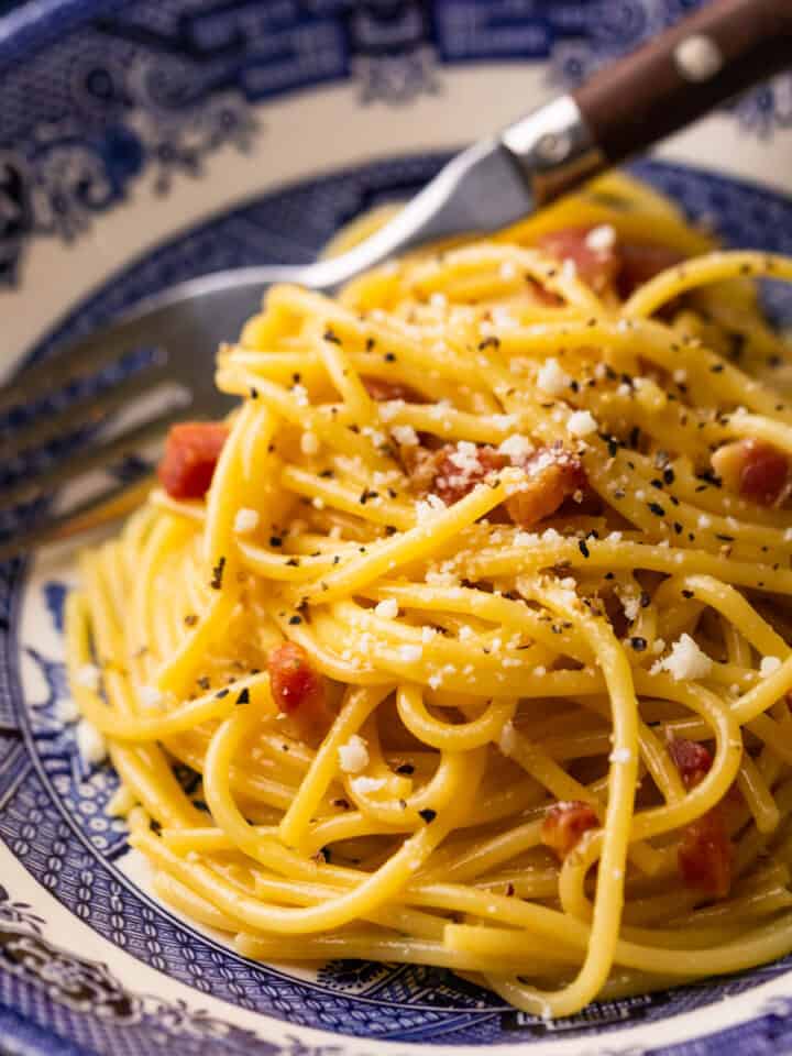 spaghetti carbonara topped with grated cheese in a blue bowl with a fork.