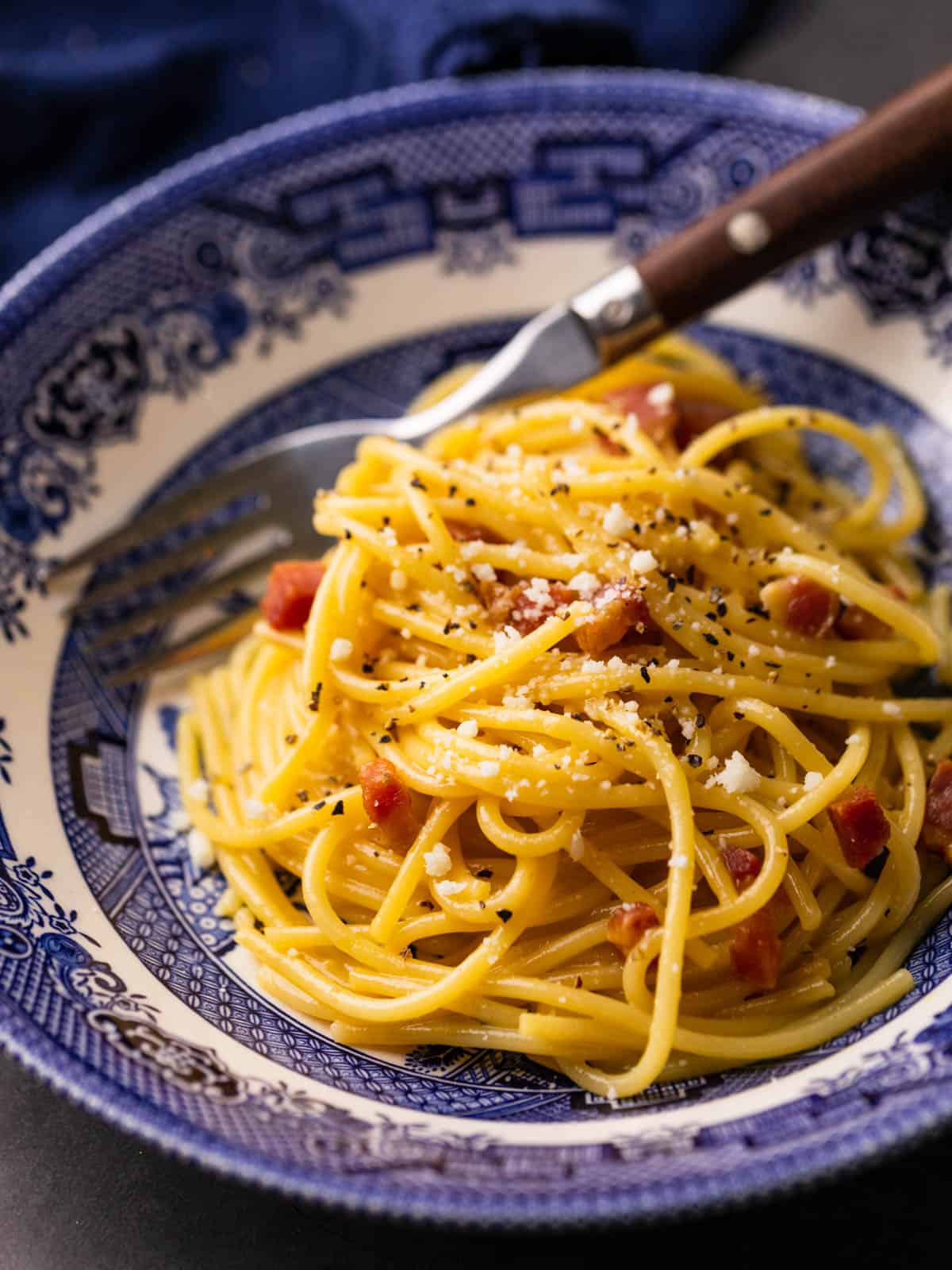 spaghetti with carbonara sauce, pancetta and grated cheese on top in a blue and white bowl.