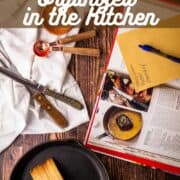 kitchen knives and cooking utensils on a table with a cook book and skillet.