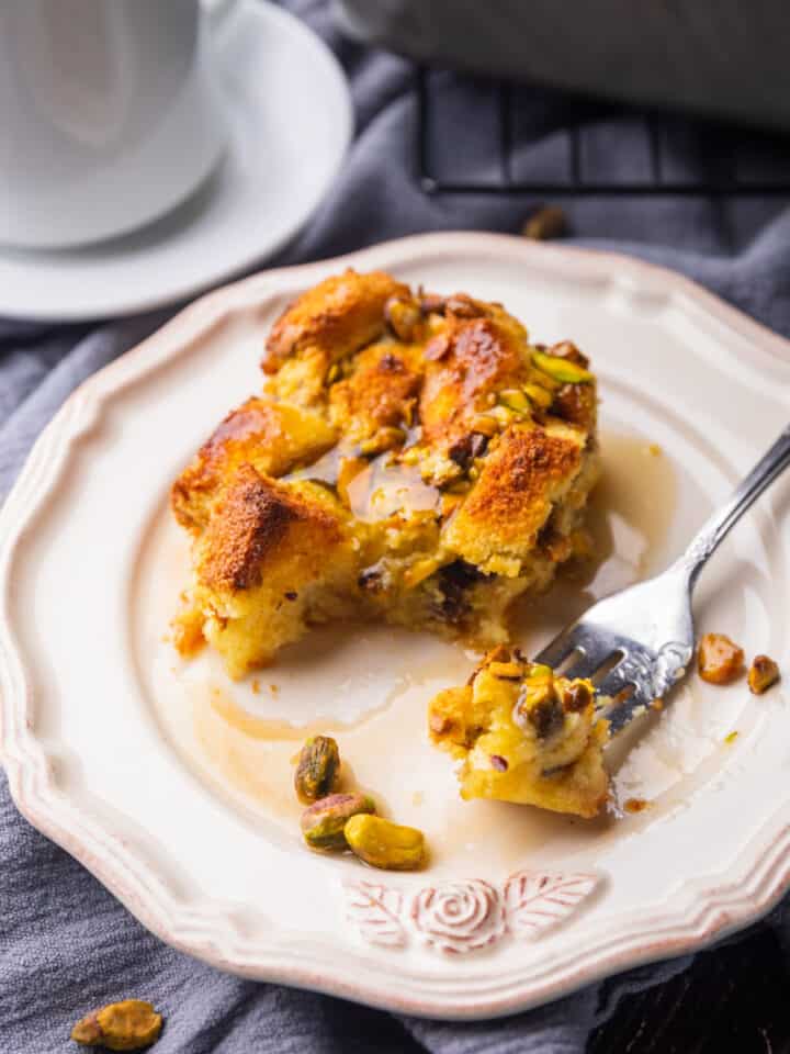 piece of bread pudding with pistachios on a plate with a bite on a fork.