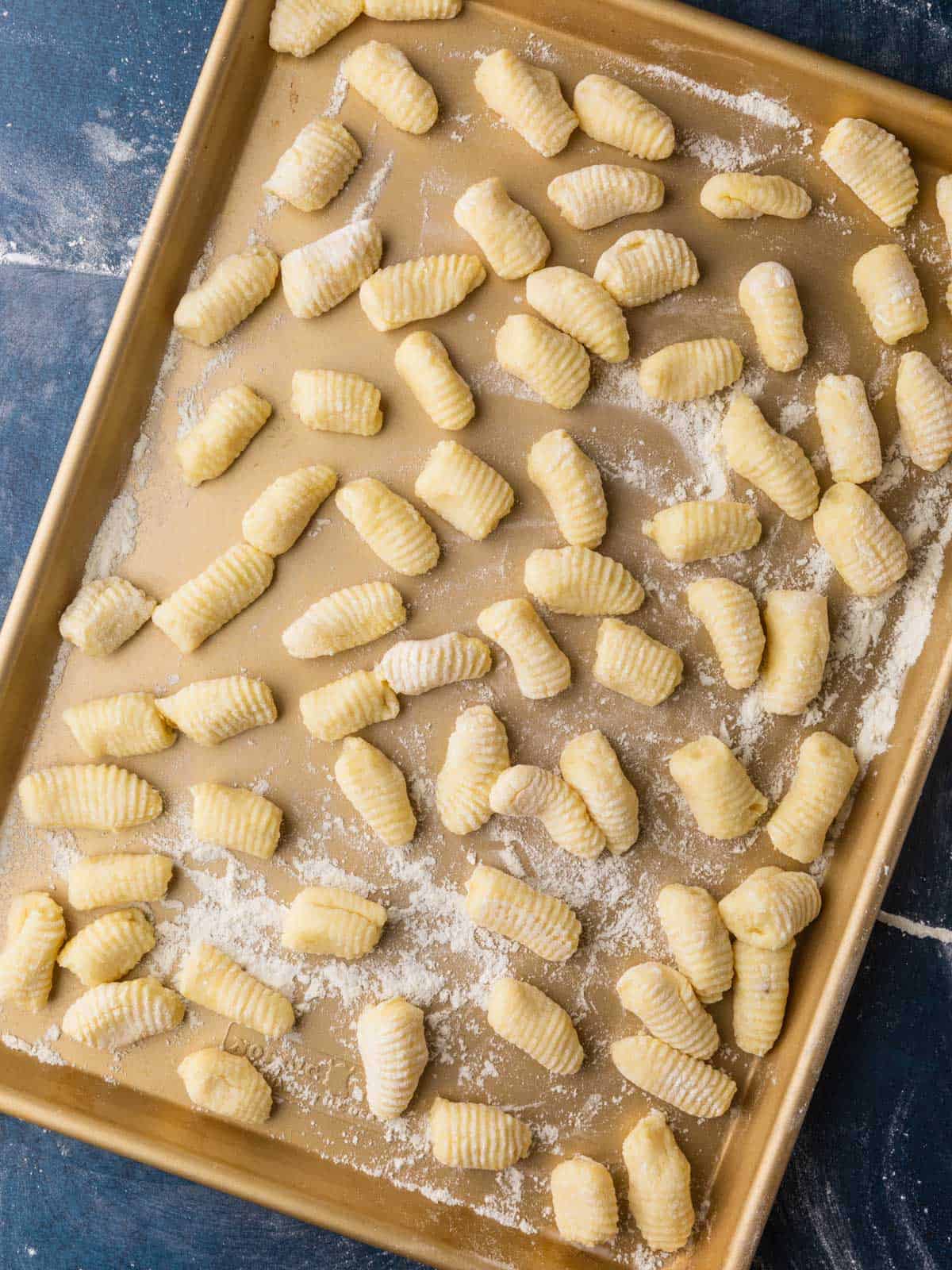 fresh shaped gnocchi on a gold floured sheet pan on a blue table. 
