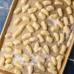 fresh italian gnocchi shaped on a floured gold sheet pan before cooking.
