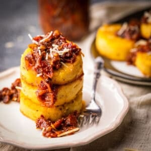 stack of fried polenta circles with tomato bacon jam and shredded parmesan.