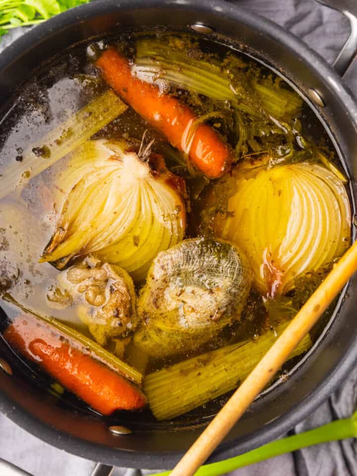 pot with beef stock and vegetables in it with wooden spoon resting on top.