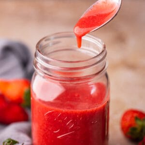 fresh strawberry puree dripping off a spoon into a mason jar.