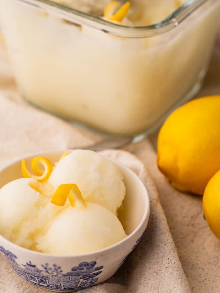 three scoops of lemon sorbet in a bowl with lemon twists on top.