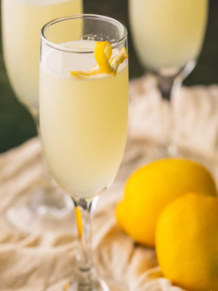 champagne flute with yellow drink garnished with lemon twist on the edge.