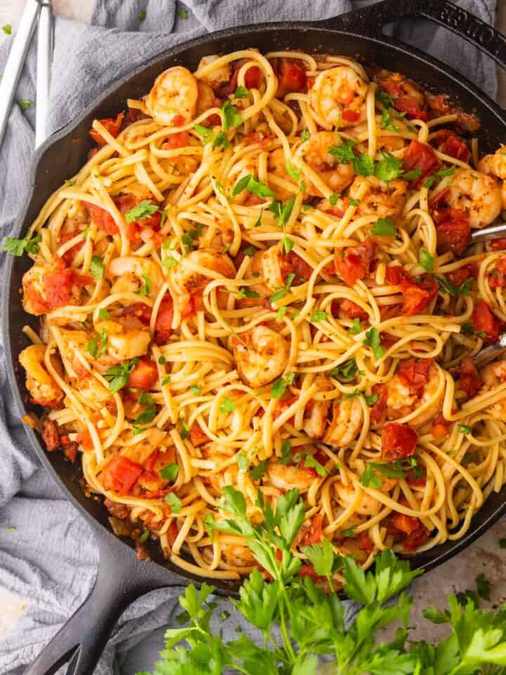 shrimp and tomato sauce with linguine and chopped parsley in a cast iron skillet with tongs.