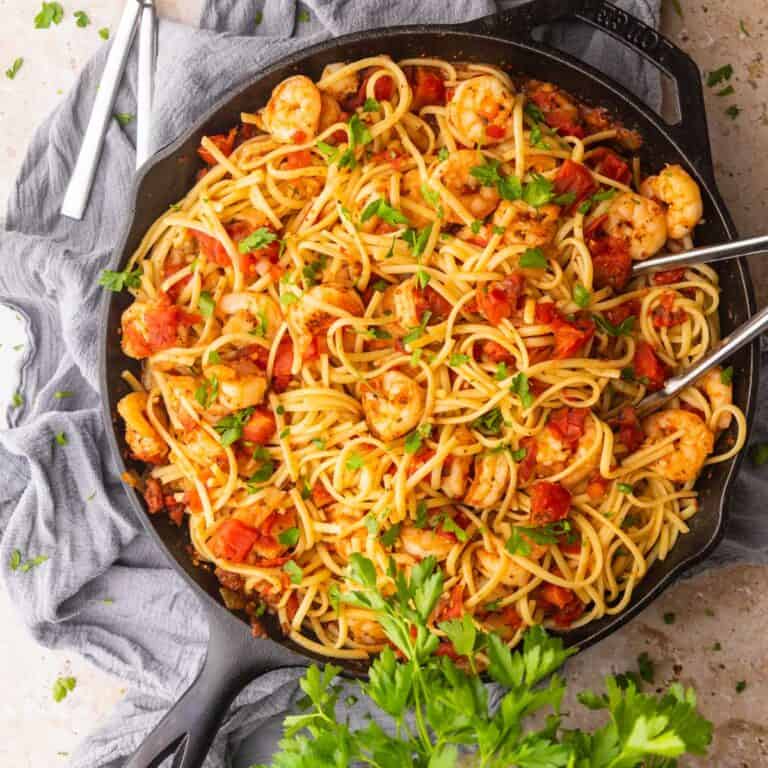 shrimp and tomato sauce with linguine and chopped parsley in a cast iron skillet with tongs.