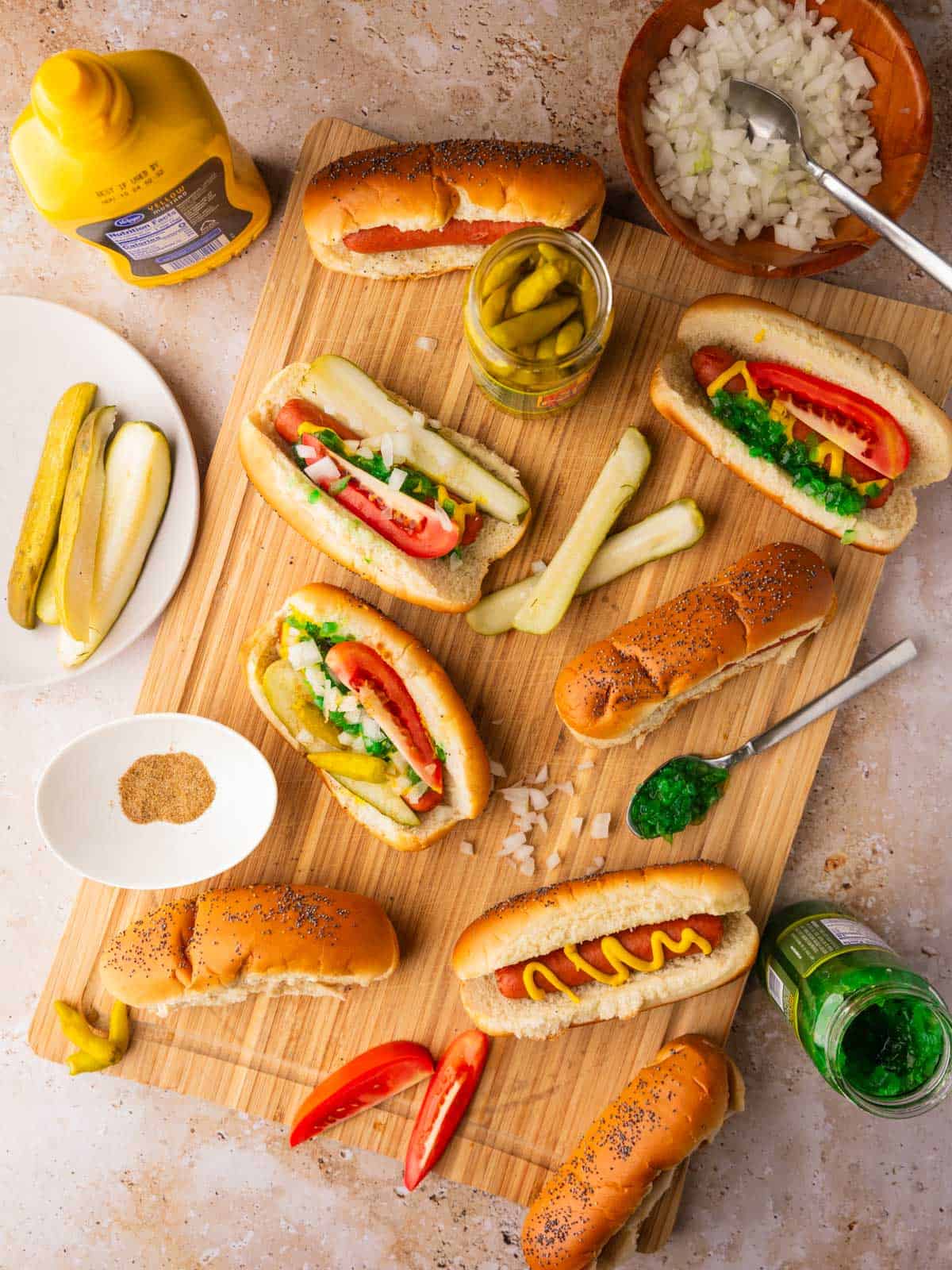 hot dogs on cutting board with some toppings on them and around in bowls and containers.