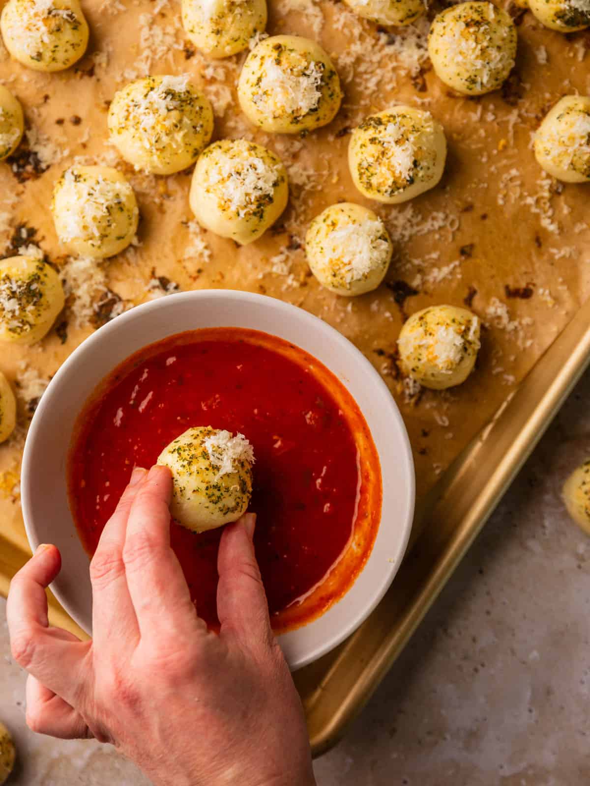 hand dipping cheese topped bread bites into marinara pizza dip.
