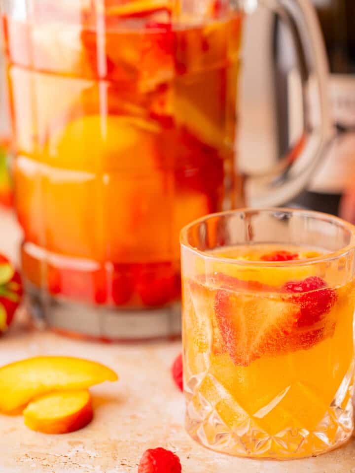 clear pitcher and glass full of white sangria with strawberries, raspberries and peaches.