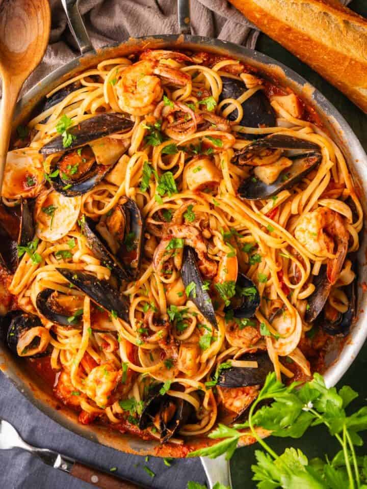 skillet of linguine with red sauce and seafood in it topped with fresh parsley.