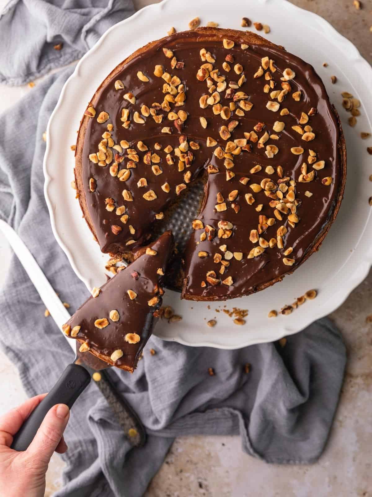 chocolate nutella cheesecake with chopped hazelnuts on a top with a slice being removed from it.