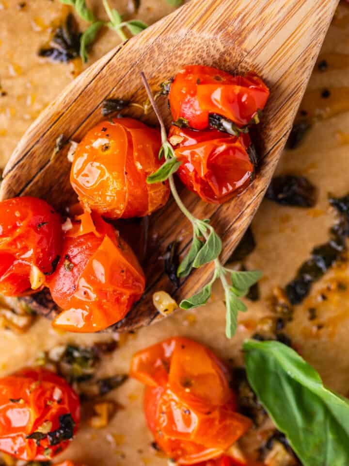 wooden spoon holding a scoop of roasted cherry tomatoes on a sheet pan with fresh thyme.