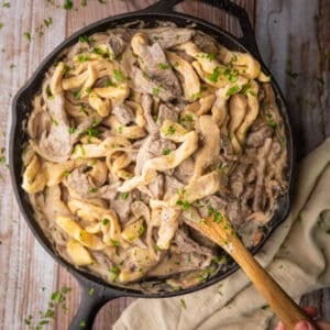 beef stroganoff with homemade egg noodles in a cast iron skillet with a wooden spoon.