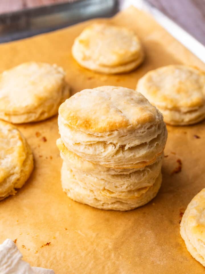 flaky biscuits on a sheet pan with some stacked on top of each other.
