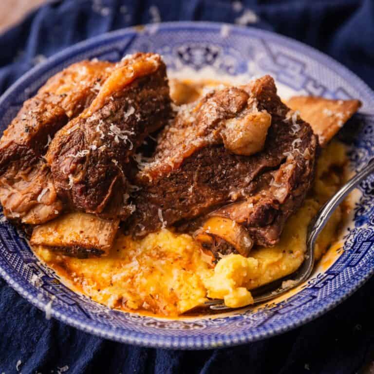 braised beef short ribs on top of polenta in a blue and white bowl with fork.