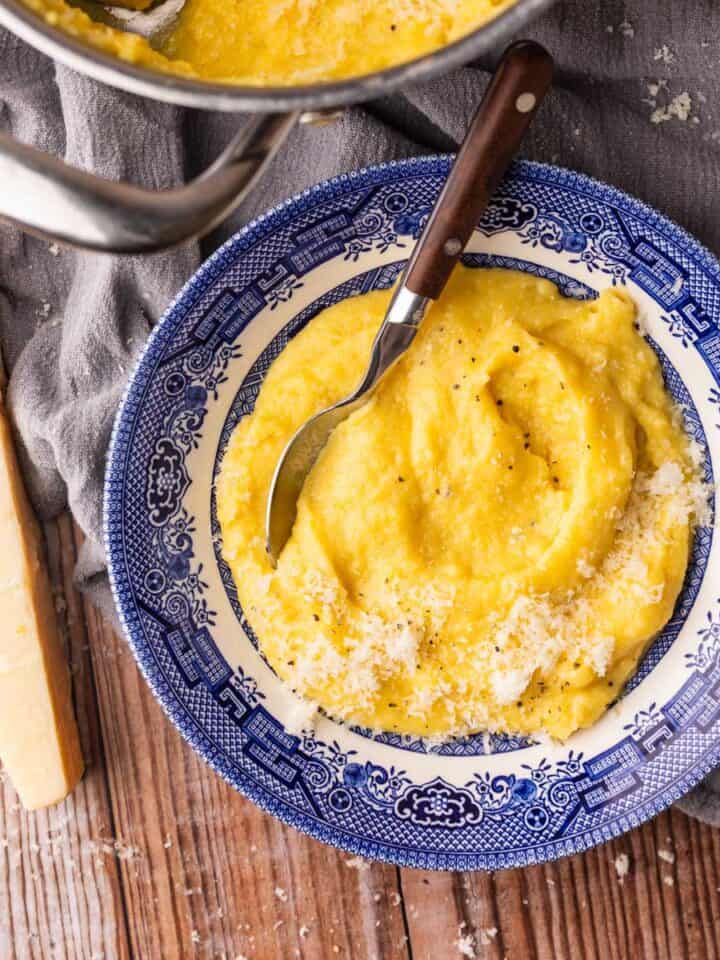 blue and white bowl filled with polenta topped with parmesan with a spoon in it.