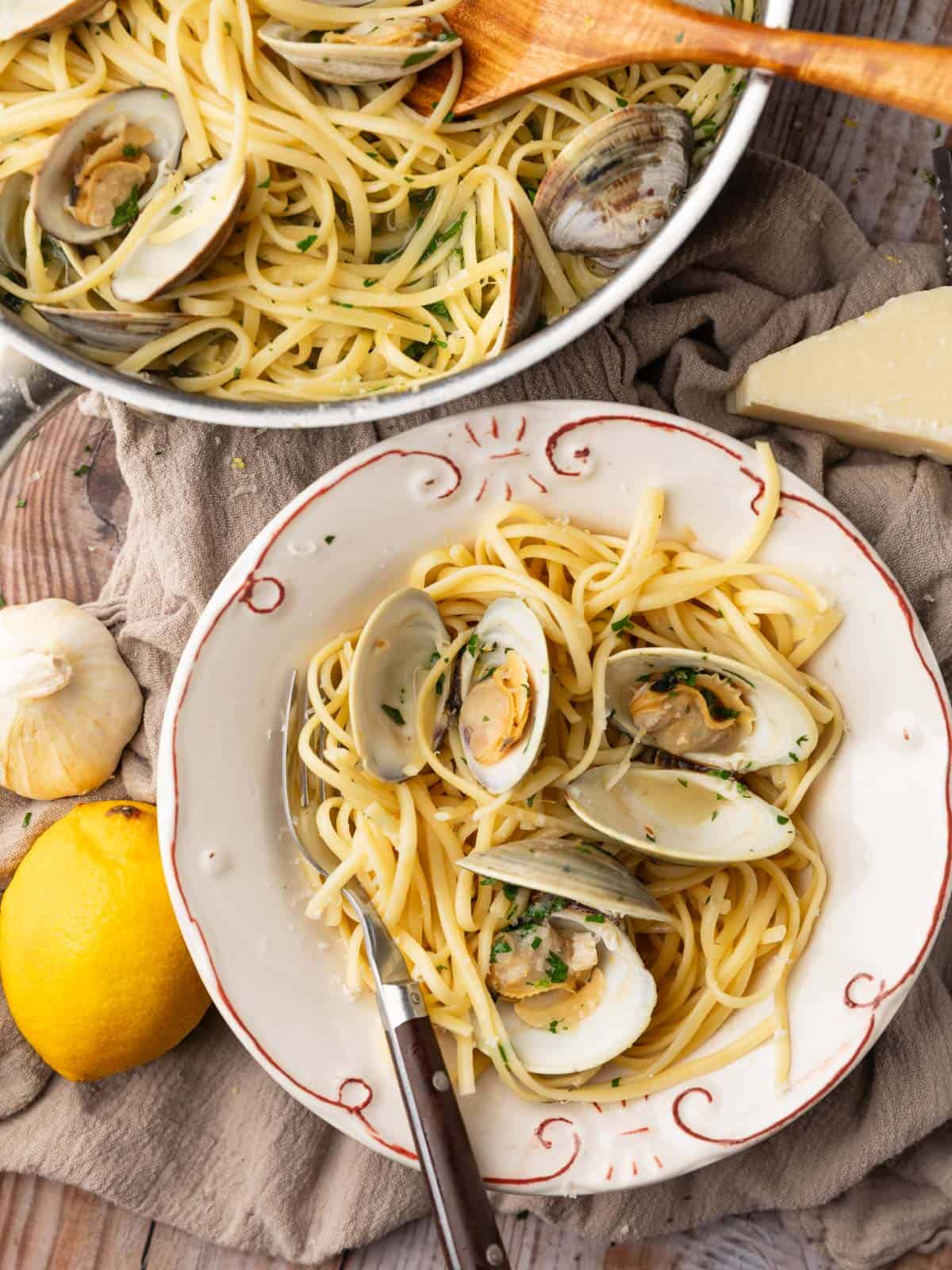 pan and bowl of linguine pasta with clams with garlic, parmesan and lemon next to it.