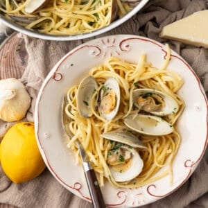 bowl of linguine with clams with a fork and lemon and garlic next to it.