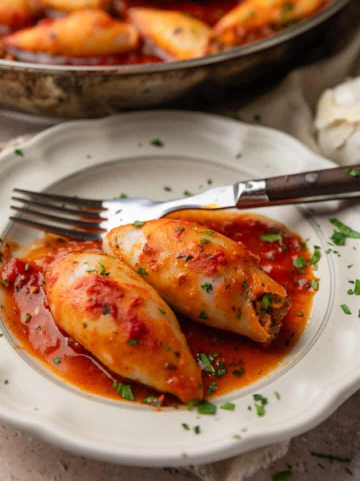 two stuffed calamari tubes covered in red sauce on a plate with a fork.