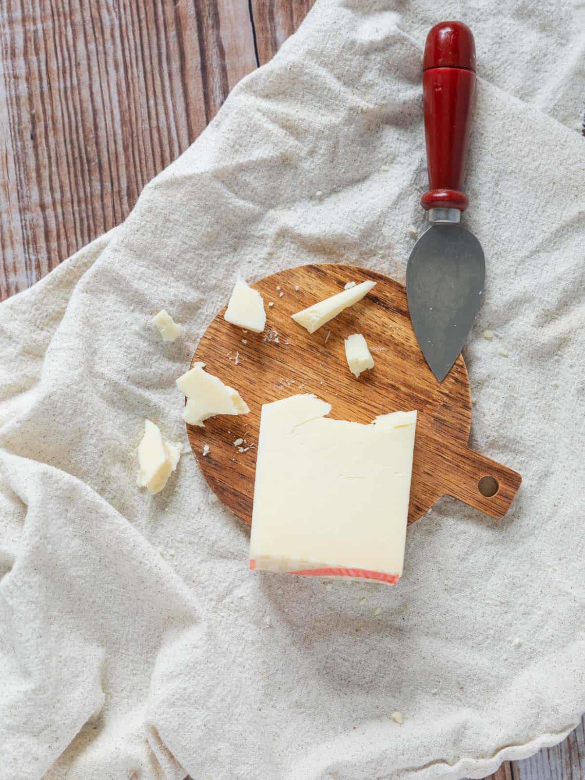 partially broken up wedge of aged italian provolone cheese on a small wooden circle with a cheese knife.