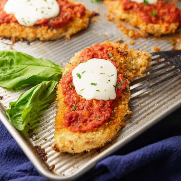 baked chicken parmesan on a sheet pan with fresh basil leaves.
