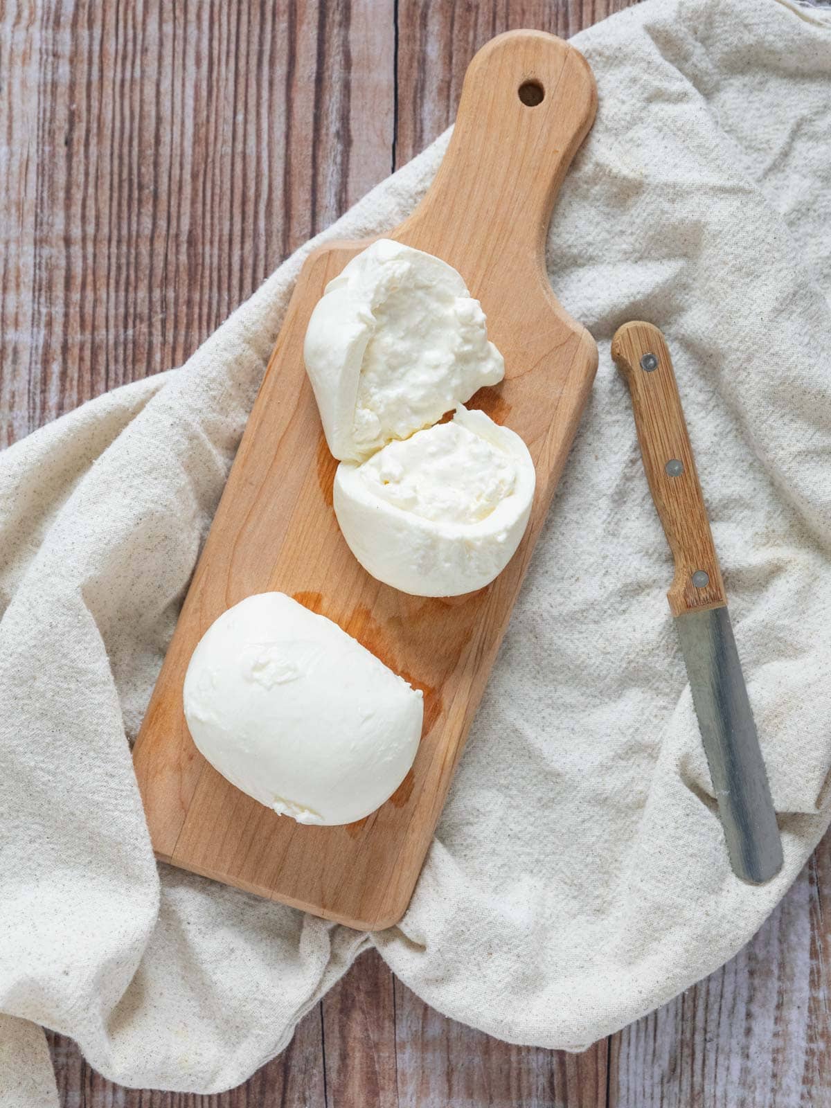 burrata cheese on a wooden cutting board, cut open to see the middle with a cheese knife.