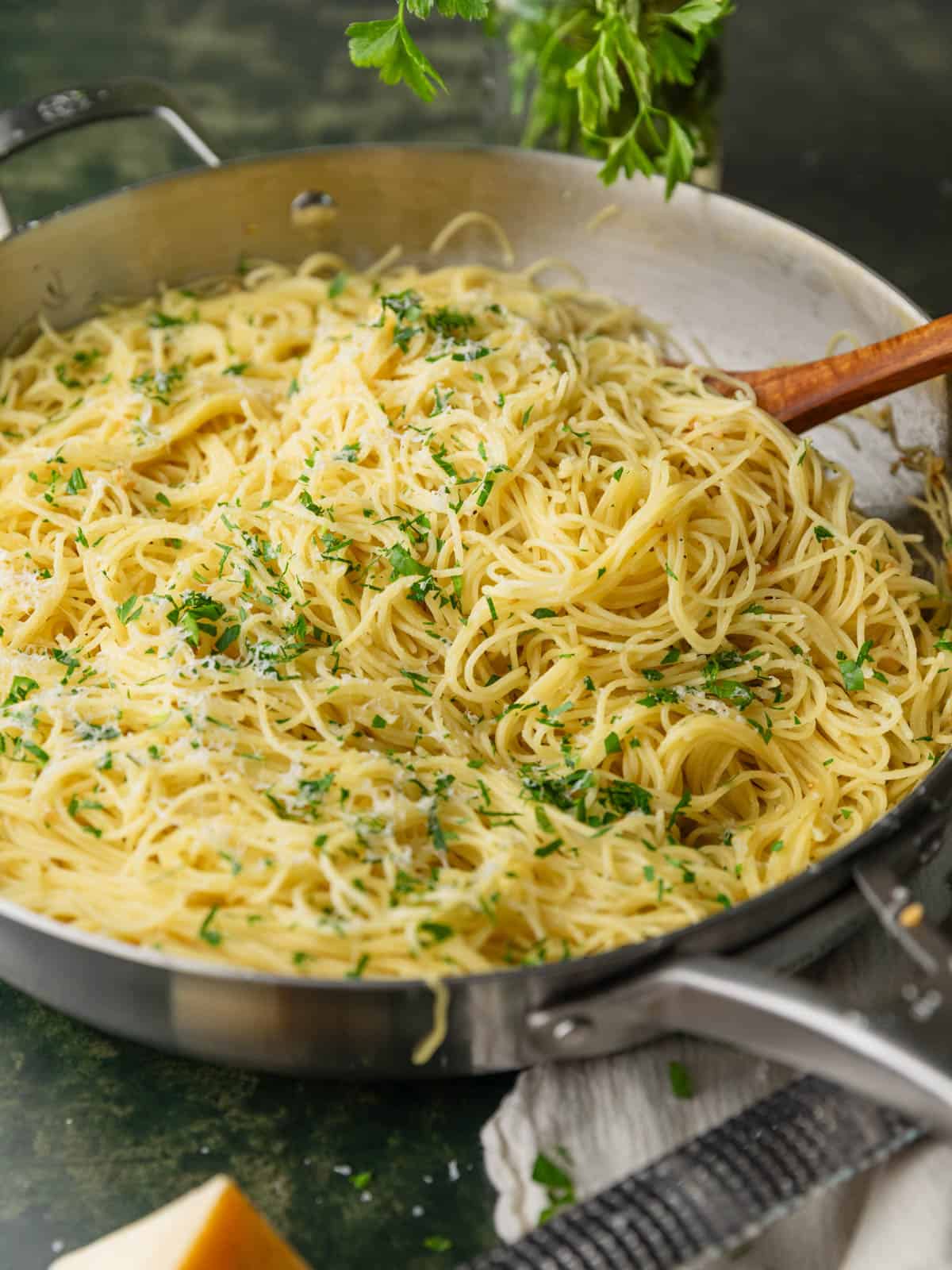 garlic butter angel hair pasta topped with chopped parsley and grated cheese in a skillet.