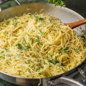 garlic butter angel hair pasta in a skillet topped with grated cheese and chopped parsley.