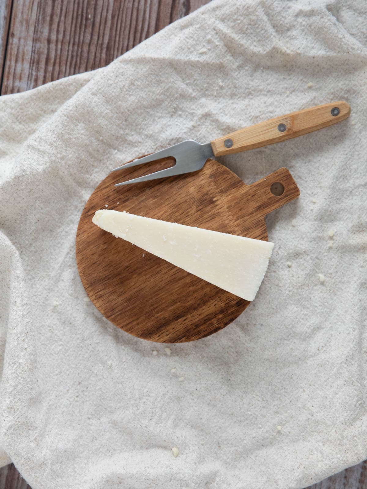 wedge of grana padano cheese on a circle wooden board with a cheese fork.