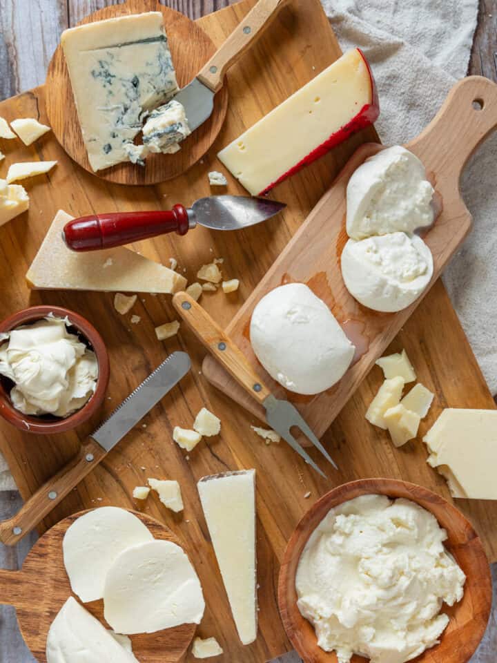 cutting board filled with various wedges and bowls of soft and hard italian cheeses.