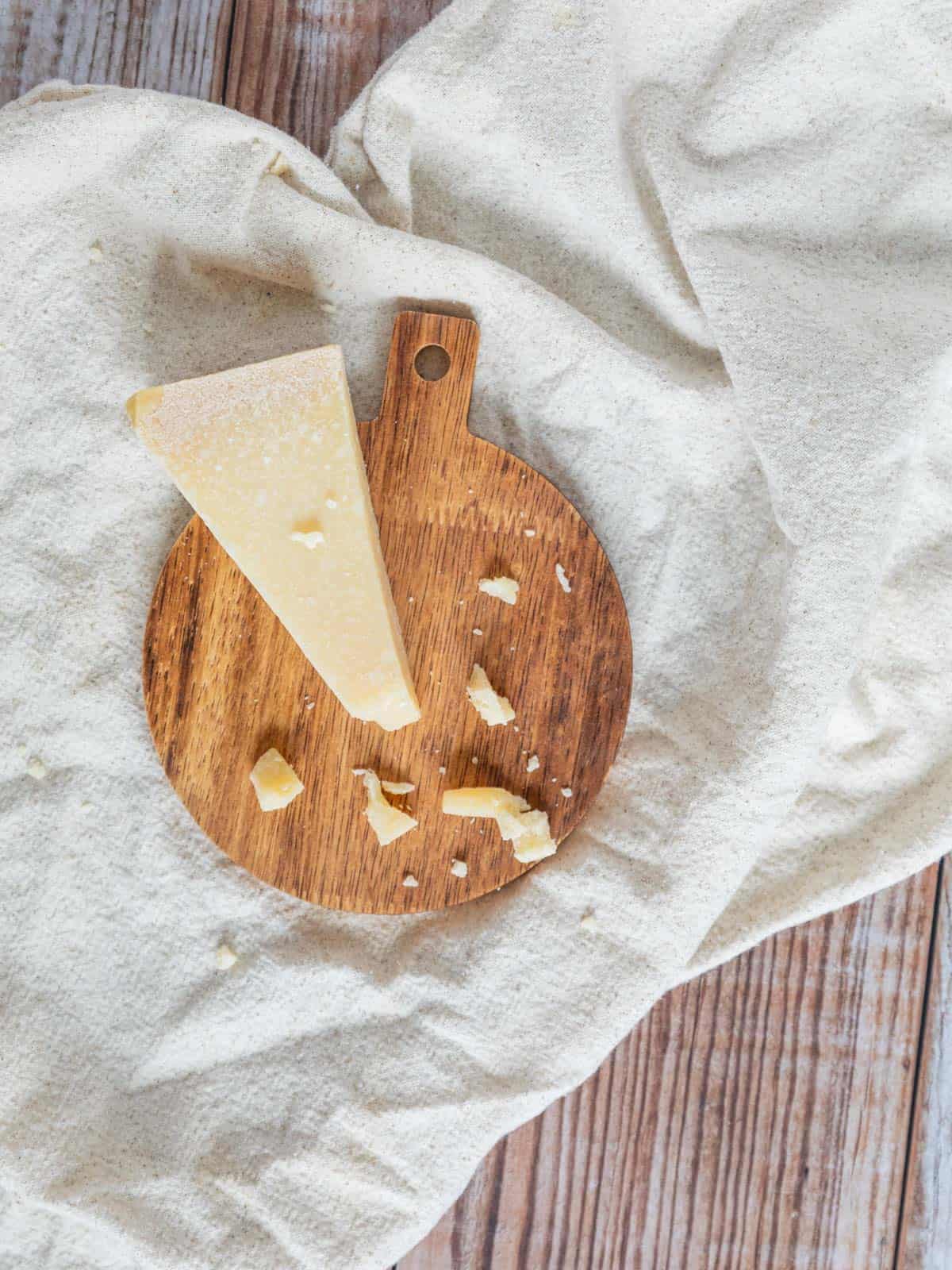 partially crumbled wedge of parmigiano-reggiano cheese on a wooden circle.