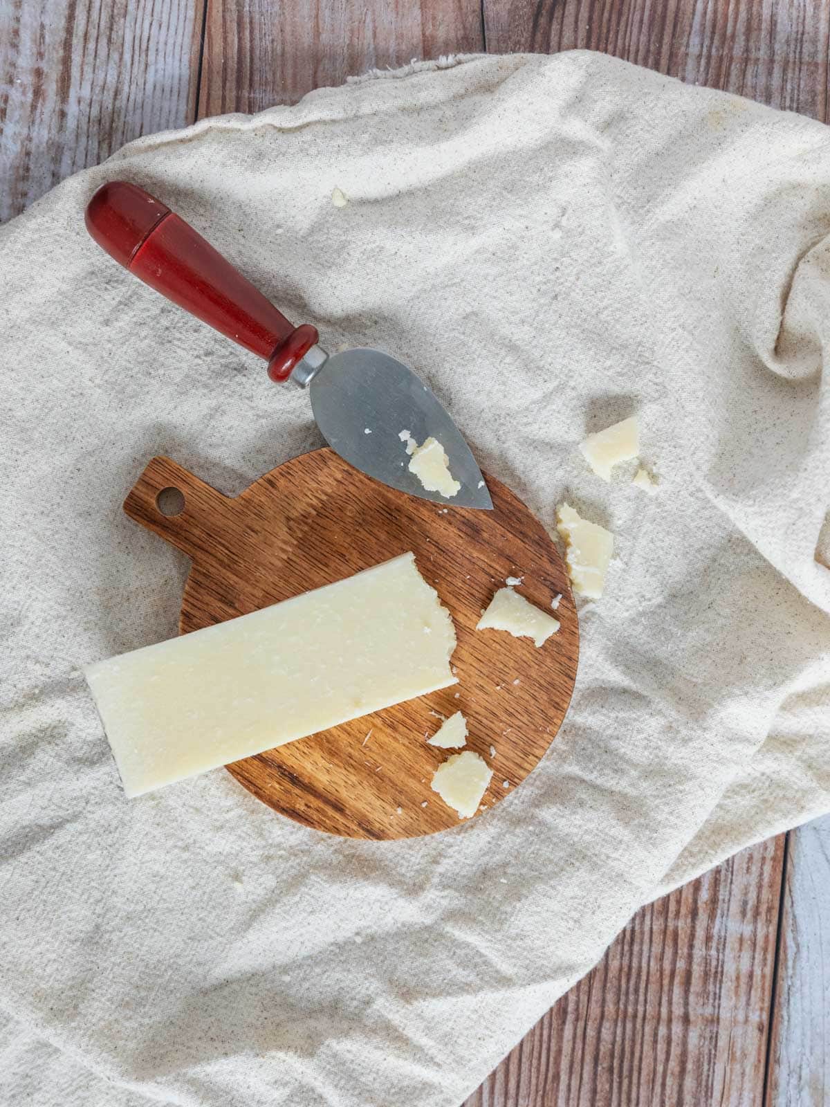 small circle cutting board with a wedge of pecorino romano cheese with a few crumbles around.