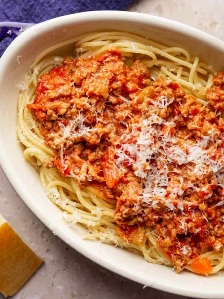 oval dish with spaghetti with bolognese sauce topped with freshly grated parmesan on top.