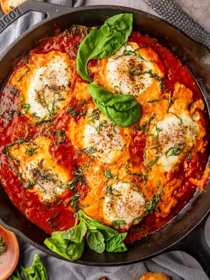 eggs baked in tomato sauce in a cast iron skillet with fresh basil leaves.