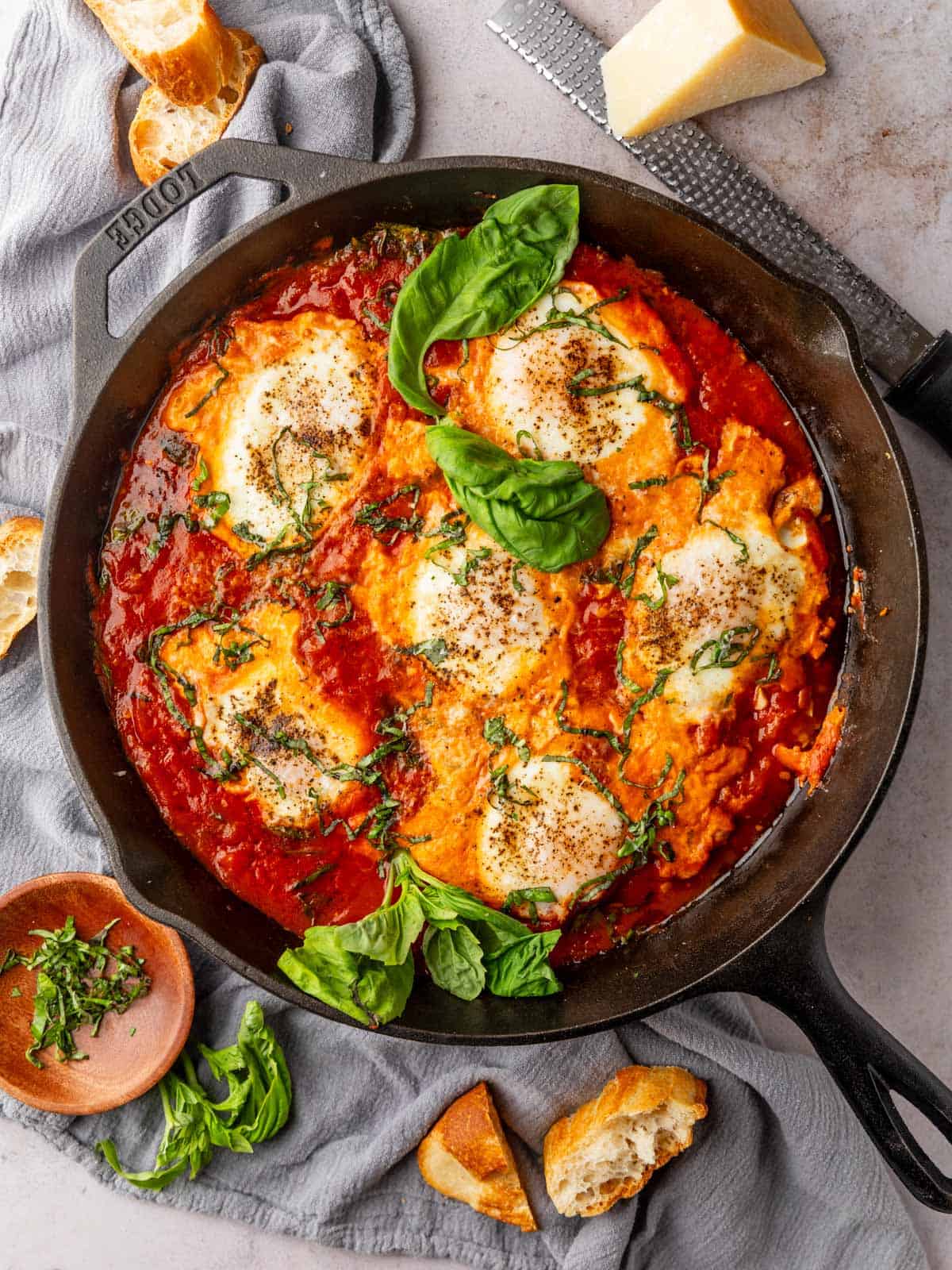 eggs baked in red sauce with in a cast iron skillet with sliced bread around it. 